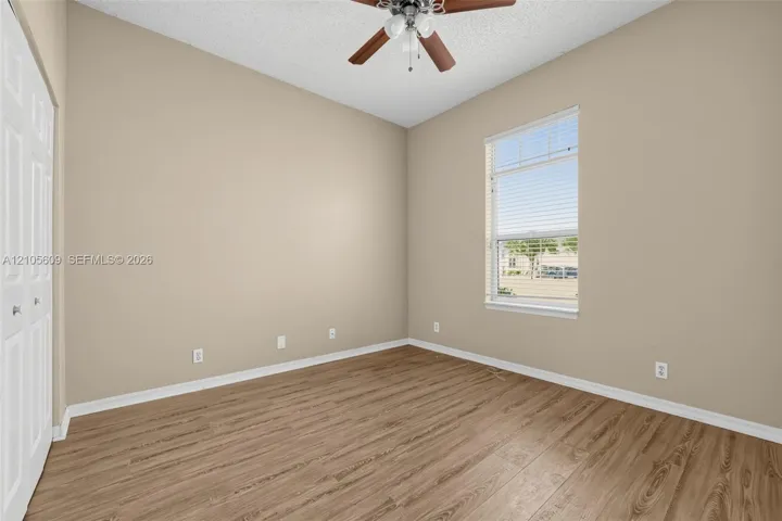 Room featuring wood-finish flooring, a ceiling fan with integrated lighting, textured ceiling, and double-door closet cabinetry