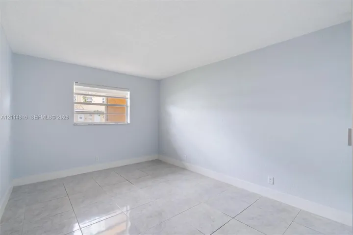 Neutral interior room featuring light-toned wall finishes, large-format tile flooring, and a horizontal louvered window