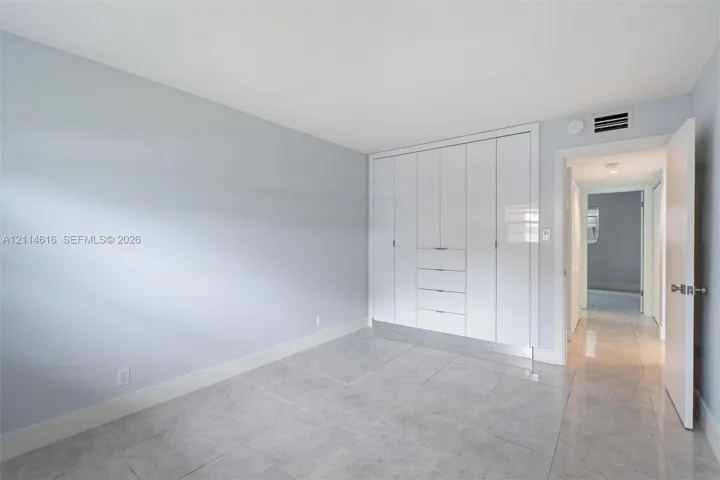 Neutral-toned room featuring large-format tile flooring and floor-to-ceiling built-in white cabinetry with integrated drawer storage