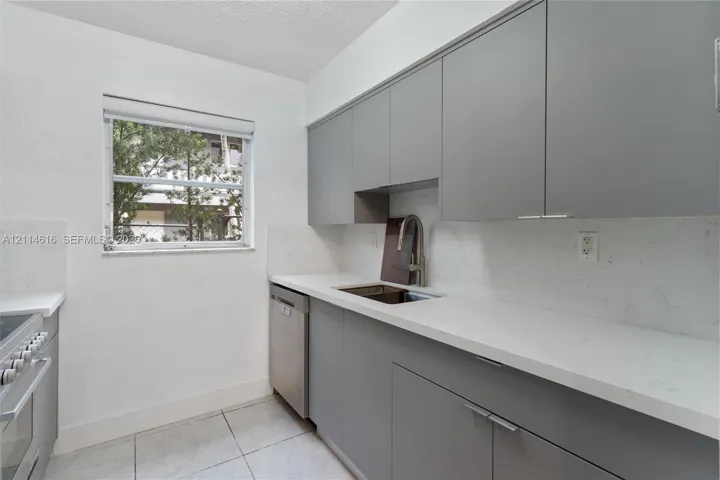 Kitchen featuring flat-panel gray cabinetry, solid-surface countertops with integrated backsplash, stainless steel dishwasher, and stainless steel pull-down faucet