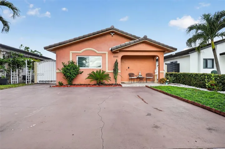 Stucco exterior featuring a covered front porch, hip roofline, decorative window molding, and expansive paved driveway
