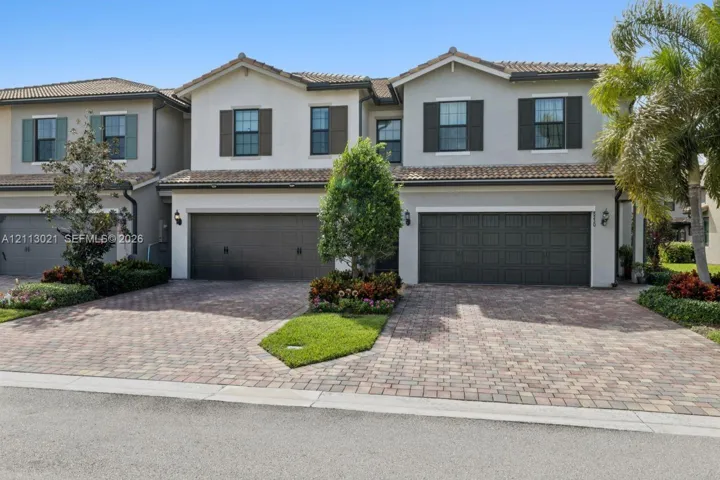 Stucco exterior featuring dual multi-car garages, decorative shutters, tile roofing, and a paved driveway