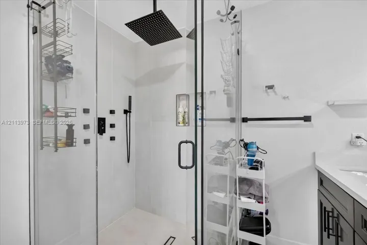 Walk-in shower featuring a frameless glass enclosure, oversized square rainfall showerhead, matte black hardware, integrated tiled niche, and light-toned wall tile
