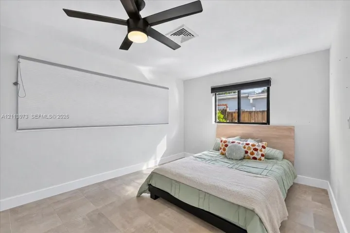 Neutral-toned tile flooring, matte black ceiling fan with integrated lighting, and dual window treatments including a roller shade and a horizontal blind
