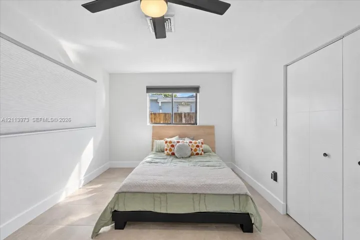 Neutral-toned tile flooring, white interior walls, ceiling fan with integrated lighting, and white multi-panel closet doors
