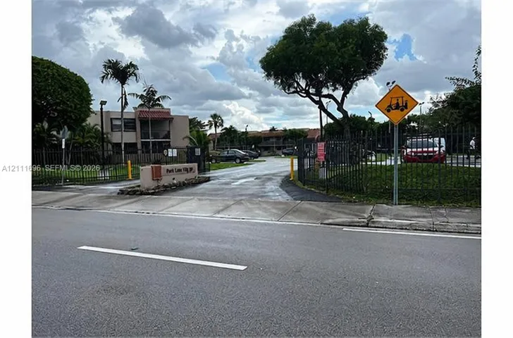 Gated community entrance featuring metal perimeter fencing, paved driveway access, and mature landscaping