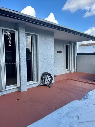 Stucco exterior featuring vertical fixed windows, a covered entryway, and a solid-surface patio floor