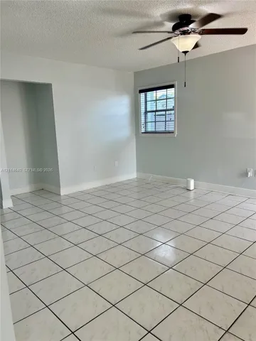 Neutral-toned interior space featuring square tile flooring, a multi-blade ceiling fan with an integrated light fixture, and a single-hung window with decorative muntins
