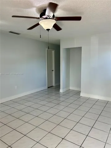 Neutral-toned room featuring large-format ceramic tile flooring, a centered ceiling fan with integrated lighting, and a textured ceiling finish