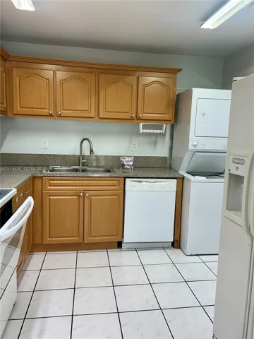 Kitchen area featuring wood cabinetry, stone-finish countertops, dual-basin sink with arched faucet, built-in dishwasher, and ceramic tile flooring