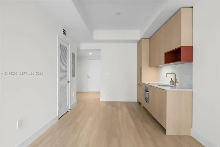 Kitchen featuring flat-panel wood-finish cabinetry, integrated oven, stone-surface countertop, brass-finish faucet, and a recessed accent shelf