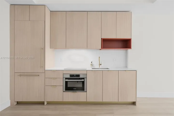 Kitchen featuring light wood-finish cabinetry, integrated refrigerator, white tile backsplash, solid surface countertop, and metallic hardware