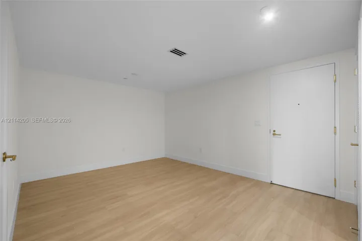 Neutral-toned room featuring light wood-finish flooring, white walls, and a white interior door with metallic hardware