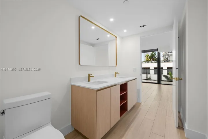Master bathroom Dual-sink vanity with light wood cabinetry, white stone countertop, rectangular undermount sinks, and gold-tone fixtures, complemented by a large gold-framed wall mirror and wood-finish tile flooring