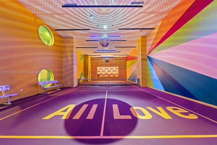Indoor pickle ball court featuring a high-contrast athletic surface, circular windows, linear ceiling lighting, mirrored spherical pendants, and custom geometric wall murals