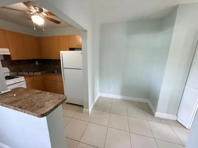 Kitchen featuring wood-finish cabinetry, stone-pattern laminate countertops, tiled flooring, and a ceiling-mounted light fixture