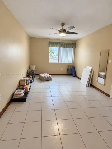 Neutral-toned interior featuring large-format ceramic tile flooring, a polished metal ceiling fan with integrated lighting, and a window with a fabric valance and vertical blinds