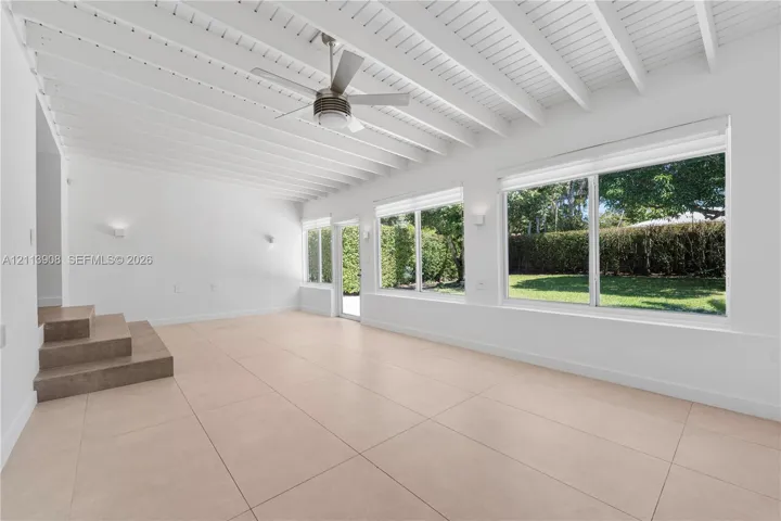 Open-concept space featuring expansive floor-to-ceiling windows, high exposed-beam ceilings, large-format tile flooring, and a central ceiling fan