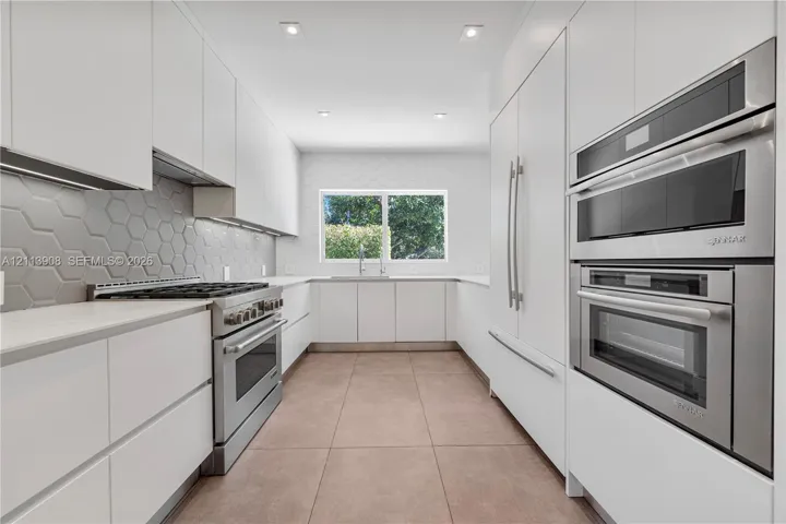 Kitchen featuring flat-panel cabinetry, stainless steel double wall ovens, a gas range, a hexagonal-pattern backsplash, and tile​​‌​​​​‌​​‌‌​‌‌​​​‌‌​‌​‌​‌​​​‌​​ flooring