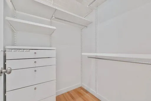 Walk-in closet featuring white built-in drawers, adjustable shelving, metal hanging rods, and wood-finish flooring