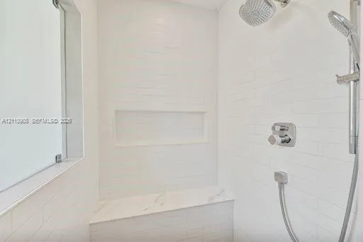 Walk-in shower featuring white subway-style wall tile, a stone-finish bench seat, an integrated wall niche, and dual-function polished chrome shower fixtures