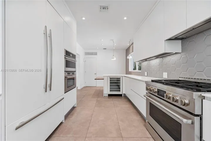 Contemporary kitchen featuring flat-panel white cabinetry, stainless steel professional-grade range, hexagonal tile backsplash, built-in wine refrigeration, and large-format tile flooring
