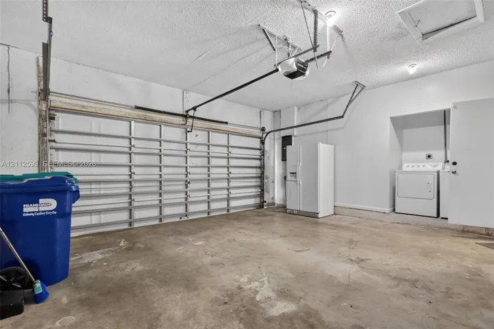 Enclosed two-car garage featuring a sectional overhead door, automatic door opener, concrete flooring, and an integrated laundry utility area