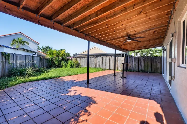 Covered outdoor patio featuring tile flooring, a natural wood-finish ceiling with an integrated ceiling fan, and fenced backyard grounds