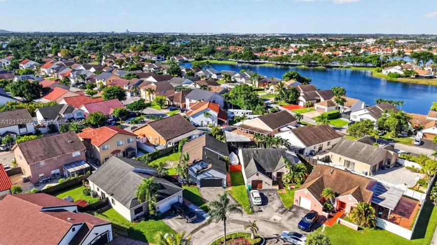 Aerial perspective of a residential neighborhood featuring multi-pitch roofs, paved driveways, manicured lawns, and proximity to a large community lake