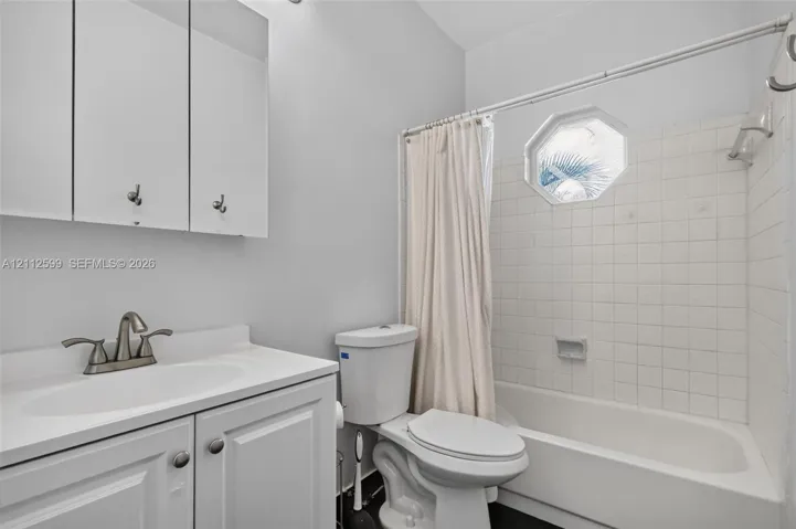 Bathroom featuring a vanity cabinet with integrated countertop, octagonal window, white ceramic tile tub surround, and a wall-mounted mirrored medicine cabinet