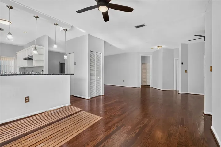 Open floor plan featuring wood-finish flooring, a kitchen peninsula with pendant lighting, and ceiling fan fixtures