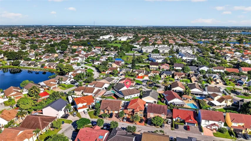 Aerial perspective of a suburban neighborhood featuring residential dwellings, street infrastructure, and proximity to a large body of water