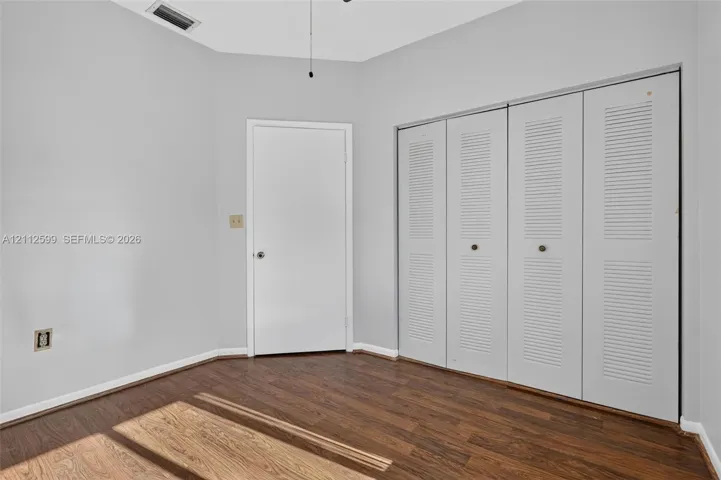 Interior room featuring wood-finish flooring, neutral wall paint, and floor-to-ceiling closet cabinetry with white louvered bifold doors