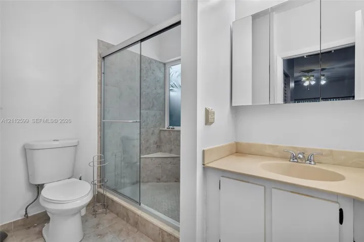 Bathroom featuring a vanity with an integrated sink, neutral countertop, wall-mounted mirrored medicine cabinet, and a walk-in shower with a glass enclosure and tiled bench