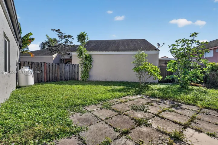 Rear exterior grounds featuring a paved stone patio, lawn area, perimeter wood fencing, and mature landscaping