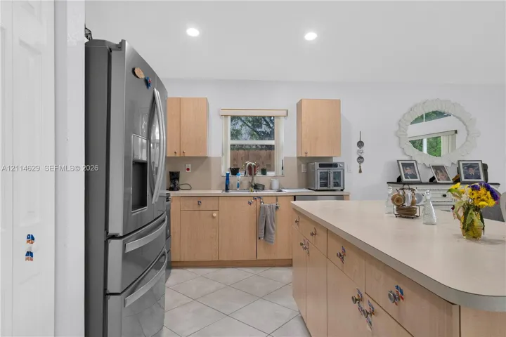 Kitchen featuring light-finish cabinetry, a central island with countertop seating, stainless steel refrigerator, tile flooring, and recessed lighting