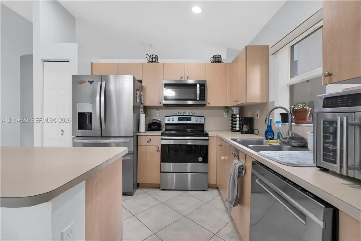 Kitchen featuring flat-panel wood cabinetry, stainless steel appliances, solid-surface countertops, dual-basin sink, and tile flooring