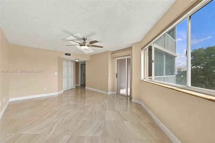 Polished stone-finish tile flooring, large sliding glass door, oversized windows with a stone-top sill, and a multi-blade ceiling fan