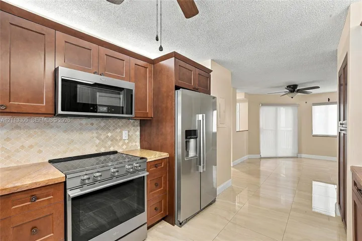 Kitchen featuring medium-tone wood cabinetry, stone countertops, stainless steel appliances, a diamond-pattern tile backsplash, and polished tile flooring