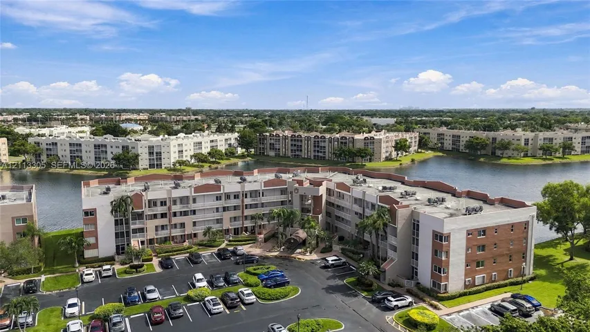 Aerial perspective of a multi-story residential building featuring masonry and stucco exterior, situated on a lakefront lot with surrounding water and landscaped green space