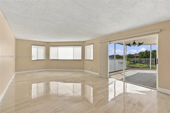 Living area featuring large-format tile flooring, expansive multi-pane windows, and a sliding glass door providing access to a screened-in balcony with ceiling fan