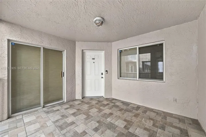 Covered entryway featuring textured wall finishes, multi-tonal ceramic tile flooring, a six-panel entry door, and a sliding glass door