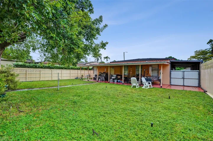 Rear exterior featuring a covered patio, fenced perimeter, mature tree, and attached carport