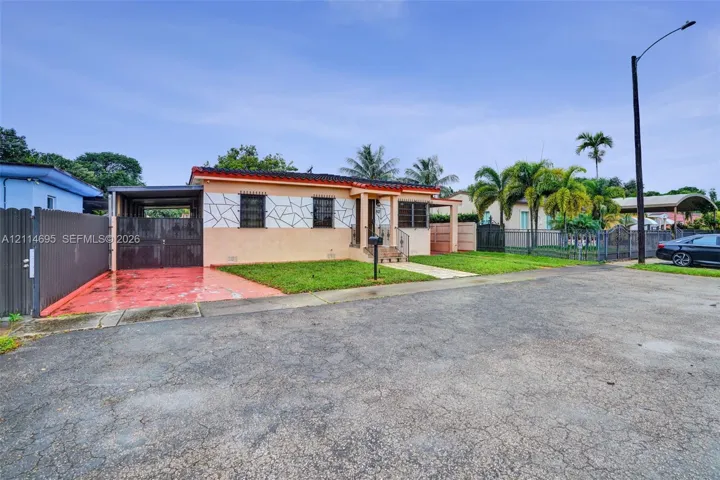 Single-story residence featuring a decorative geometric exterior facade, a covered carport, metal window security grates, and exterior masonry fencing