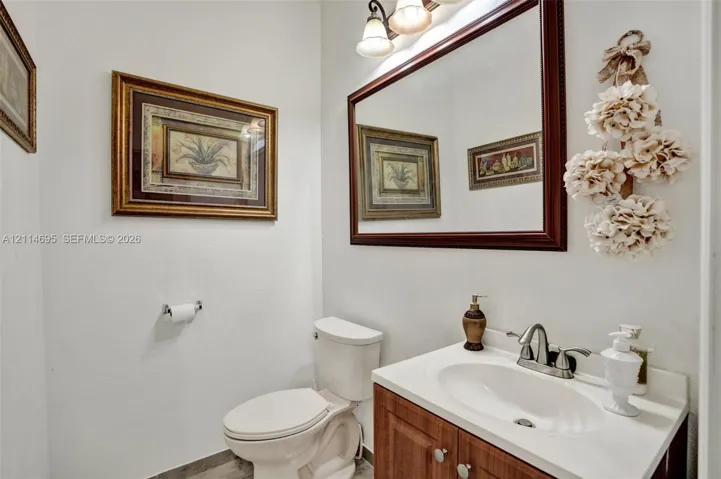 Bathroom featuring a vanity with a white composite countertop, integrated oval basin, and wood-finish cabinetry, complemented by a tri-light fixture, framed wall mirror, and two-piece toilet