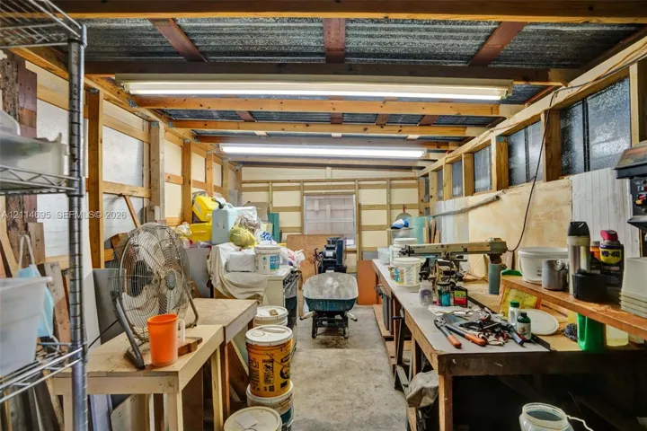 Workshop space featuring exposed timber framing, concrete flooring, corrugated metal ceiling panels, and integrated overhead fluorescent lighting