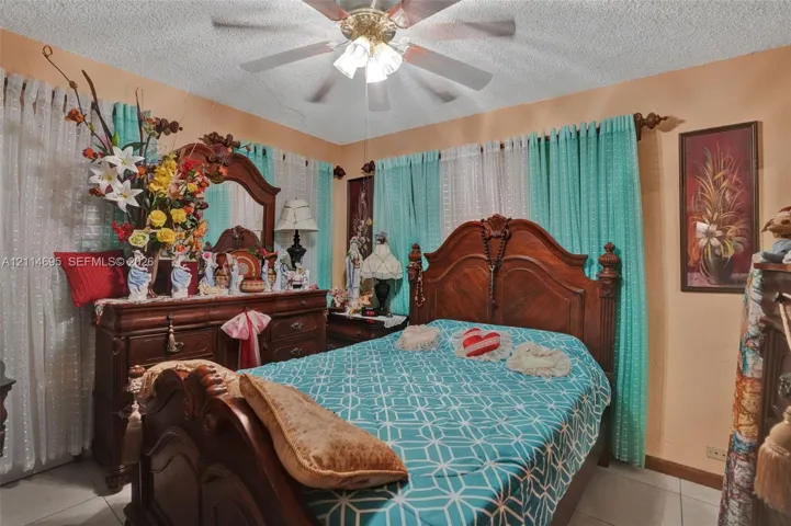 Ceiling-mounted light fixture with a multi-blade paddle fan, textured ceiling finish, and light-toned tile flooring