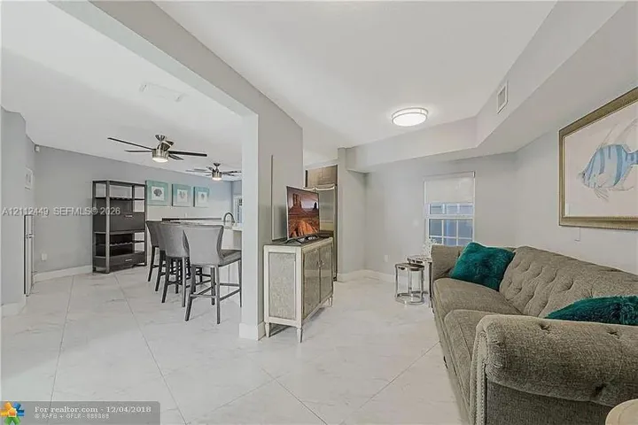 Open interior featuring light-colored tile flooring, flush-mount ceiling lighting, ceiling fans, and a kitchen peninsula