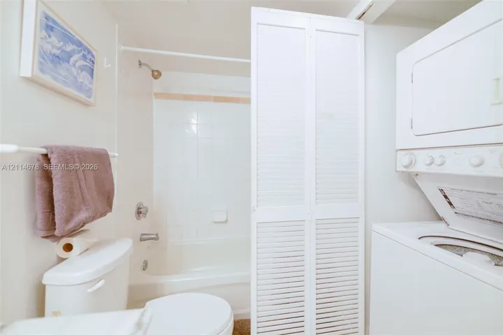 Full bathroom featuring white tile surround, tub-shower combination, and louvered bifold doors concealing a stacked laundry unit