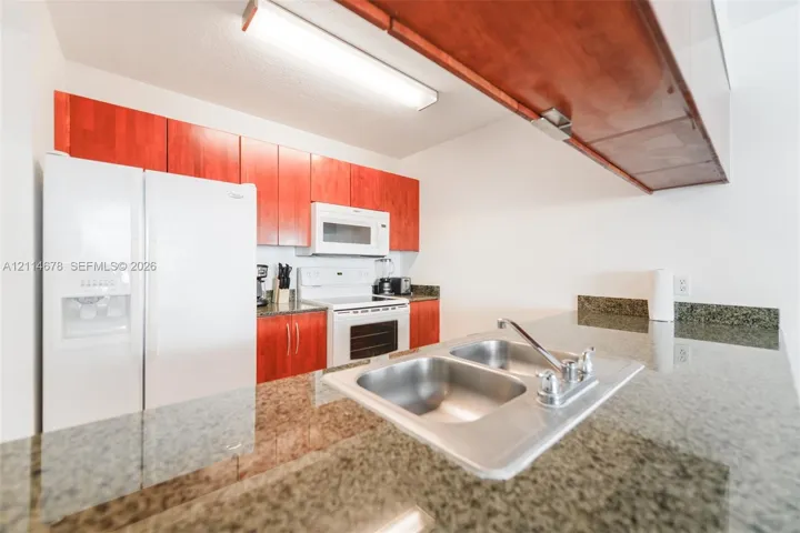 Kitchen featuring stone-finish countertops, stainless steel double-basin sink with a chrome faucet, wood-finish cabinetry, and built-in appliances including a refrigerator, microwave, and range